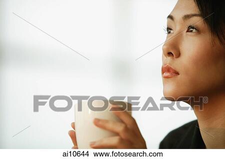 Young woman sitting at desk, holding mug View Large Photo Image Picture - Young woman sitting at desk, holding mug. Fotosearch
