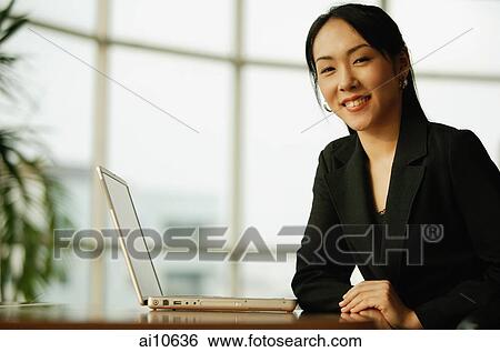 Young woman sitting at desk, looking at camera, laptop open next to her View Large Photo Image Stock Photograph - Young woman sitting at desk, looking at camera, laptop open next to her. Fotosearch