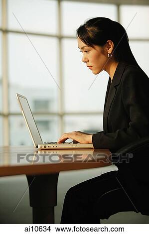Young woman sitting at desk, using laptop View Large Photo Image Picture - Young woman sitting at desk, using laptop. Fotosearch