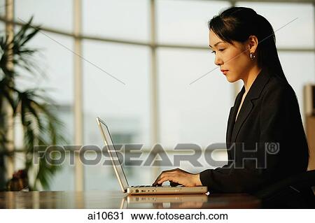 Young woman sitting at desk, using laptop View Large Photo Image Stock Image - Young woman sitting at desk, using laptop. Fotosearch