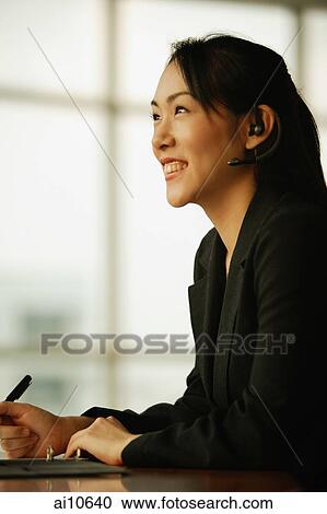 Young woman sitting at desk, using hands-free device View Large Photo Image Stock Image - Young woman sitting at desk, using hands-free device. Fotosearch