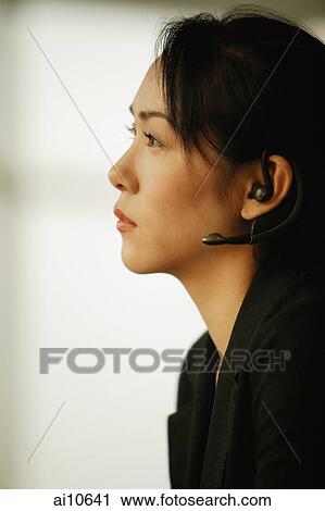 Stock Image - Young woman sitting at desk, using hands-free device. Fotosearch
