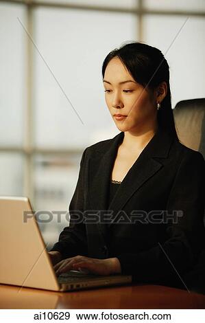 Stock Photo - Young woman sitting at desk, using laptop. Fotosearch