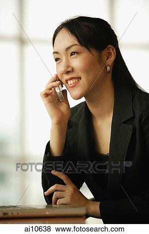 Young woman sitting at desk, using mobile phone View Large Photo Image Stock Photo - Young woman sitting at desk, using mobile phone. Fotosearch