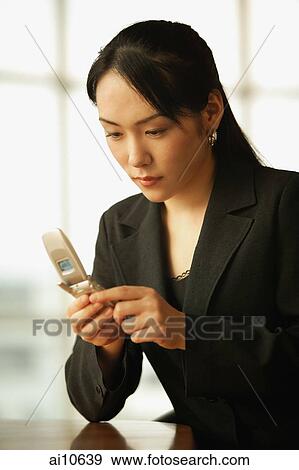 Young woman sitting at desk, using mobile phone View Large Photo Image Stock Photo - Young woman sitting at desk, using mobile phone. Fotosearch