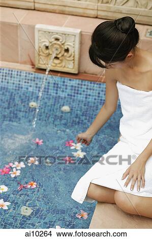 Young woman sitting by poolside touching water. View Large Photo Image Picture - Young woman sitting by poolside touching water.. Fotosearch