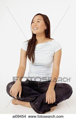 Young woman sitting cross-legged, looking off camera. View Large Photo Image Picture - Young woman sitting cross-legged, looking off camera.. Fotosearch