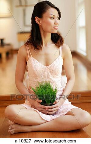 Young woman sitting cross-legged, holding plant View Large Photo Image Stock Photo - Young woman sitting cross-legged, holding plant. Fotosearch