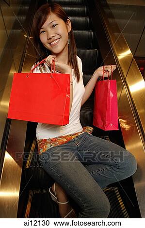 Young woman sitting escalator holding shopping bags, looking at camera View Large Photo Image Stock Image - Young woman sitting escalator holding shopping bags, looking at camera. Fotosearch