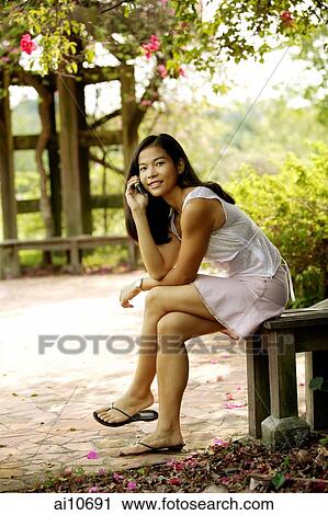 Young woman sitting on a bench, using a mobile phone View Large Photo Image Stock Image - Young woman sitting on a bench, using a mobile phone. Fotosearch