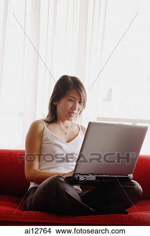 Young woman, sitting on sofa, using laptop View Large Photo Image Picture - Young woman, sitting on sofa, using laptop. Fotosearch