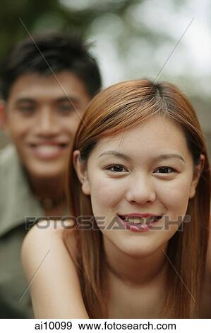 Young woman smiling, looking at camera, young man in the background View Large Photo Image Stock Photo - Young woman smiling, looking at camera, young man in the background. Fotosearch