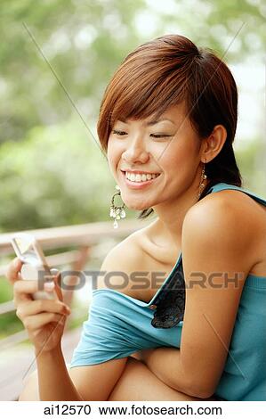 Young woman smiling, looking at mobile phone View Large Photo Image Stock Image - Young woman smiling, looking at mobile phone. Fotosearch