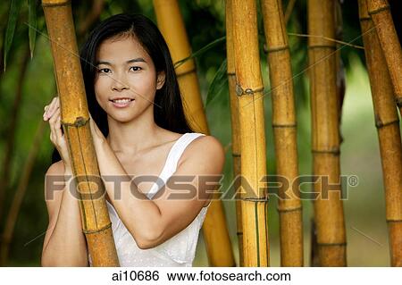 Stock Photograph - Young woman standing amongst bamboo canes, smiling. Fotosearch