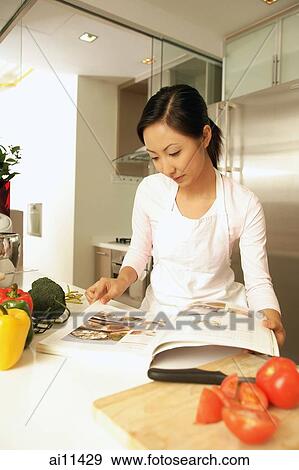 Young woman standing at kitchen counter, looking at cookbook View Large Photo Image Stock Photo - Young woman standing at kitchen counter, looking at cookbook. Fotosearch