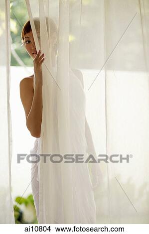 Picture - Young woman standing behind curtain, peeking. Fotosearch