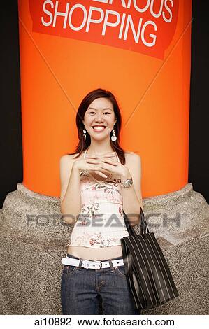 Young woman standing, looking at camera, hands clasped View Large Photo Image Stock Image - Young woman standing, looking at camera, hands clasped. Fotosearch