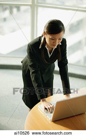 Young woman standing, using laptop View Large Photo Image Stock Photograph - Young woman standing, using laptop. Fotosearch