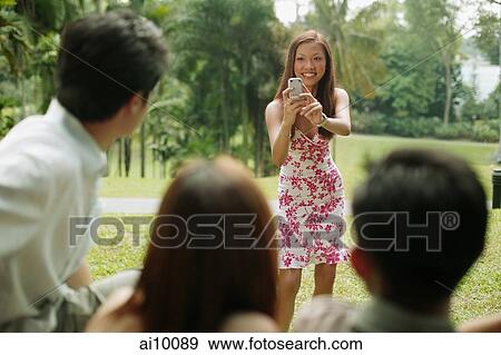 Stock Photo - Young woman taking a picture of her friends. Fotosearch