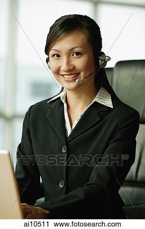Young woman using laptop and wearing hands-free device, looking at camera View Large Photo Image Stock Image - Young woman using laptop and wearing hands-free device, looking at camera. Fotosearch