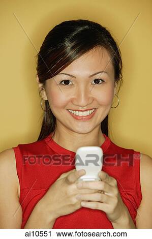 Stock Image - Young woman wearing a red top, holding a mobile phone. Fotosearch