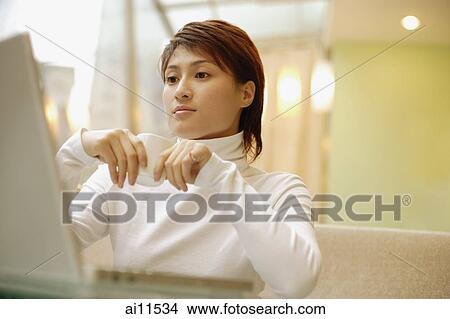 Picture - Young woman wearing white turtleneck, using laptop. Fotosearch