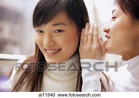 Stock Image - Young woman whispering to another woman. Fotosearch