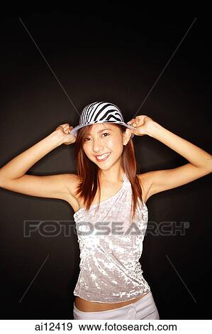 Stock Photo - Young woman with hat, hands on head, looking at camera. Fotosearch