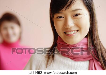Stock Image - Young woman with scarf smiling, another woman in background. Fotosearch