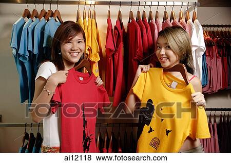 Young women at clothes shop holding up T shirts View Large Photo Image Stock Photo - Young women at clothes shop holding up T shirts. Fotosearch