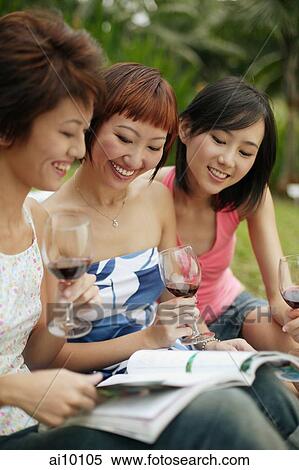 Stock Photography - Young women browsing through magazine, wine glasses in hand. Fotosearch