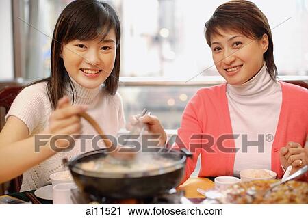 Stock Image - Young women having soup at restaurant, looking at camera. Fotosearch