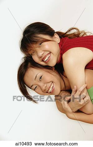Stock Image - Young women hugging, looking at camera. Fotosearch
