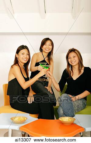 Stock Photo - Young women, looking at camera and holding cocktails. Fotosearch