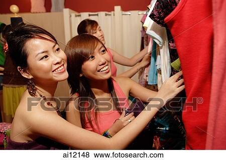 Stock Photo -  Young women looking at clothes on clothes rack. Fotosearch