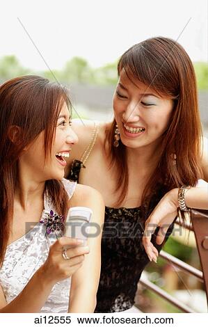 Young women looking at each other, one holding mobile phone View Large Photo Image Stock Photography - Young women looking at each other, one holding mobile phone. Fotosearch