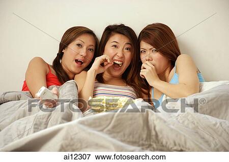 Young women lying on bed side by side, eating popcorn View Large Photo Image Stock Photo - Young women lying on bed side by side, eating popcorn. Fotosearch