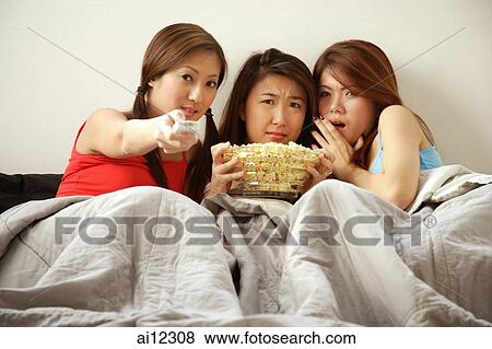 Young women lying on bed watching TV View Large Photo Image Stock Photo - Young women lying on bed watching TV. Fotosearch