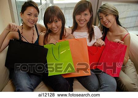 Young women sitting on sofa, side by side, holding shopping bags View Large Photo Image Stock Photo - Young women sitting on sofa, side by side, holding shopping bags. Fotosearch