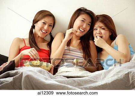 Young women sitting side by side, eating popcorn and watching TV View Large Photo Image Stock Photo - Young women sitting side by side, eating popcorn and watching TV. Fotosearch