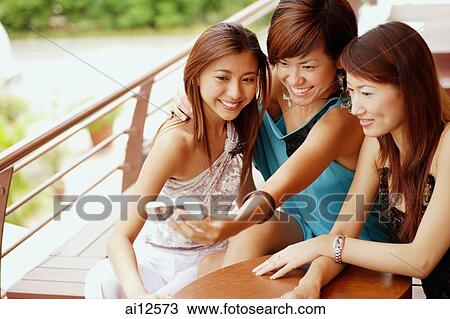 Young women sitting side by side, using camera phone View Large Photo Image Stock Image - Young women sitting side by side, using camera phone. Fotosearch