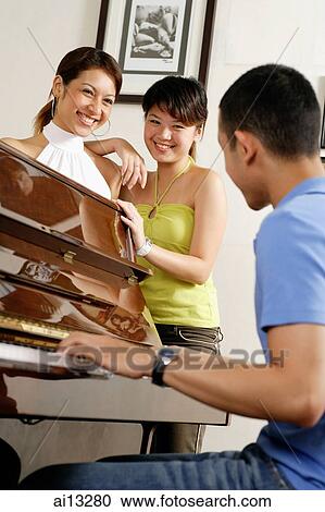 Young women standing watching young man playing the piano View Large Photo Image Stock Image - Young women standing watching young man playing the piano. Fotosearch