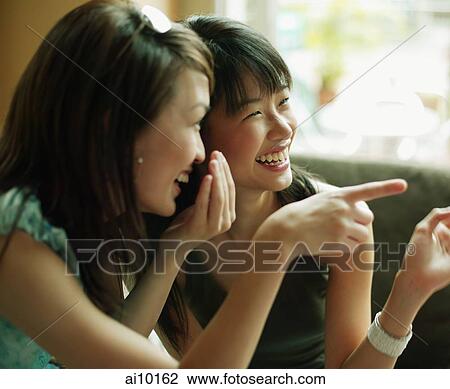 Stock Image - Young women whispering and pointing.. Fotosearch