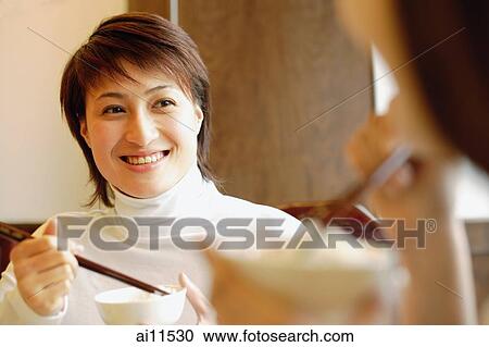 Stock Image - Young women with bowls and chopsticks, eating.. Fotosearch