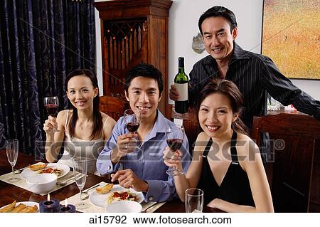Stock Image - Adults at dining table, smiling at camera, raising wine glasses. Fotosearch