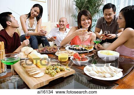 Picture - Adults having a party in living room, food on coffee table. Fotosearch