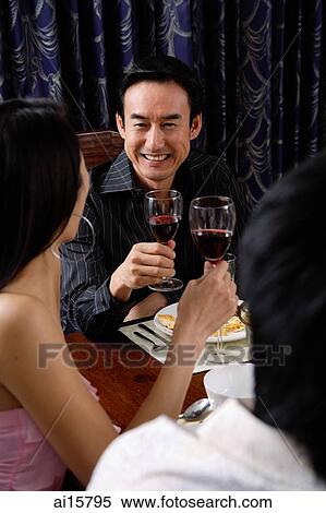 Stock Photography - Adults holding wine glasses, sitting at table. Fotosearch