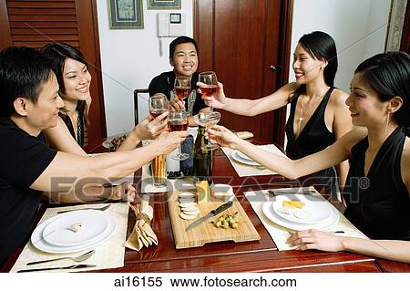 Stock Photography - Adults sitting at dining table toasting with wine glasses. Fotosearch