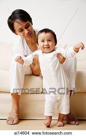 Baby boy standing, mother supporting him, looking away View Large Photo Image Picture - Baby boy standing, mother supporting him, looking away. Fotosearch
