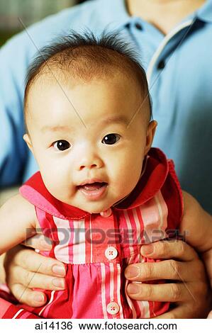 Stock Photograph - Baby girl looking at camera, father carrying her. Fotosearch